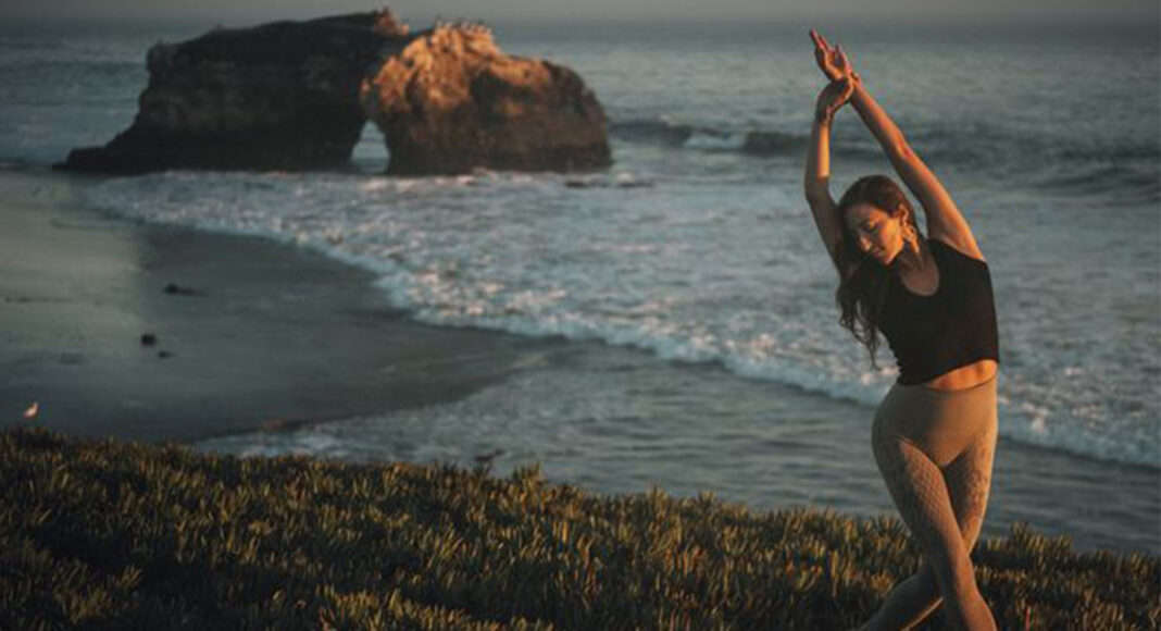 Divinitree Yoga teacher Magnolia Rasa stretches at Natural bridges State Beach.