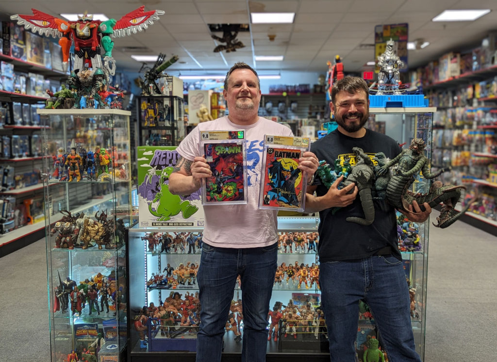 Two men holding up comics at toys in a collectibles shop