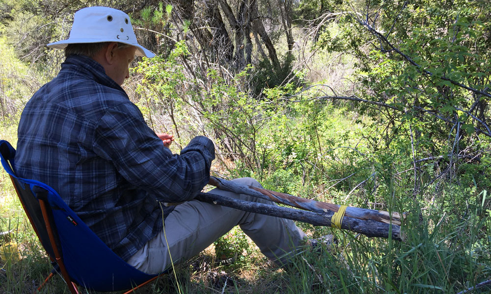 Man making a crutch while sitting in the wilderness