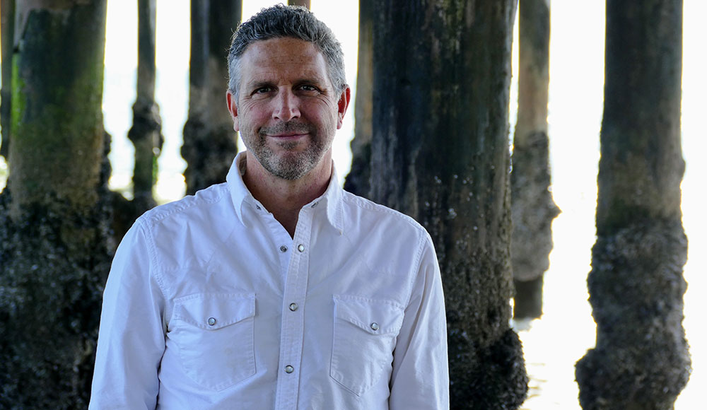 Man standing in front of pilings under a pier