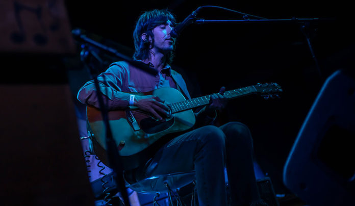 Local DIY Label Shallow Dive Releases Benefit Compilation Person playing guitar onstage, dark background with blue highlights