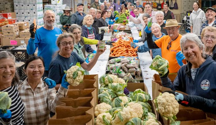 Seniors Helping Seniors Group of people lined up on both sides of a long table covered with vegetables