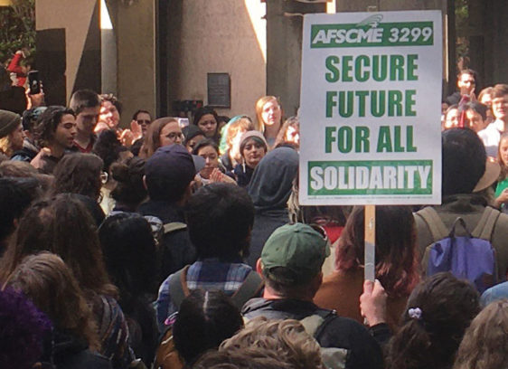 Workers in the UC System Remain Without a New Contract Crowd of protestors with a union sign reading "Secure Future for All"