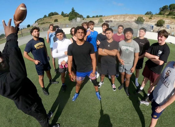 Pro Baller Reggie Stephens Gives Back Man holding up a football by a group of youths on an athletic field