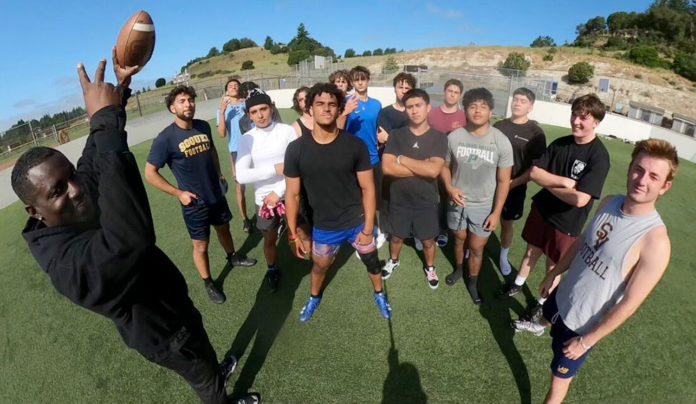 Pro Baller Reggie Stephens Gives Back Man holding up a football by a group of youths on an athletic field