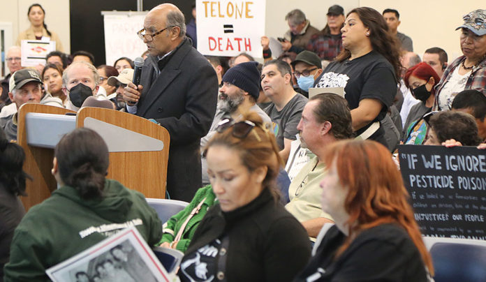 Something in the Air Man speaking at a meeting with people holding up signs