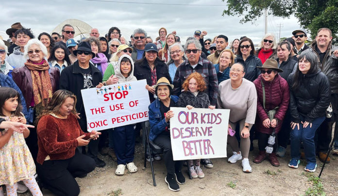 Activist Dolores Huerta Speaks Out Against Pesticide Use People at an outdoor meeting with signs