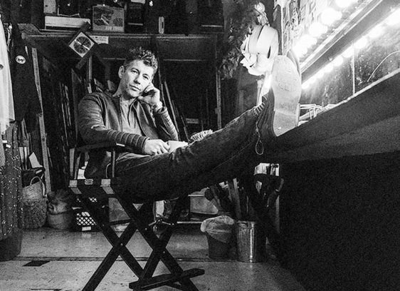 Tragedy + Time Black-and-white photo of a guy backstage with his feet propped up