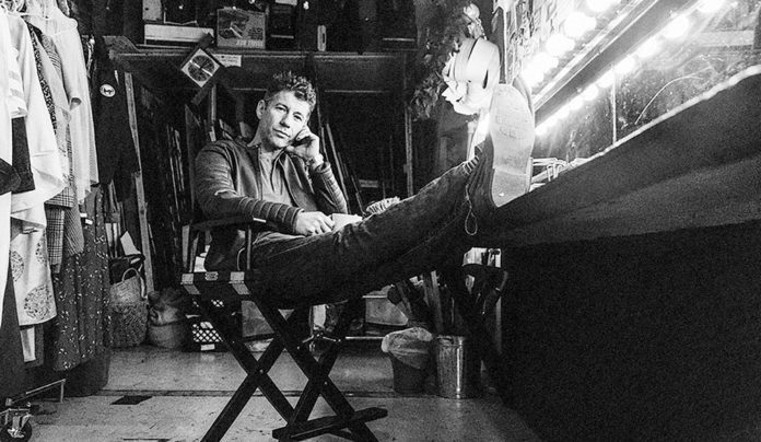 Tragedy + Time Black-and-white photo of a guy backstage with his feet propped up
