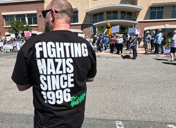 Collective Action Man at a rally wearing a shirt that says “Fighting Nazis Since 1996”