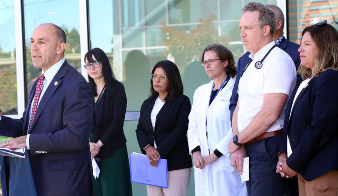 Health Providers Sound Alarm About OBBBA Cuts Group of people around man talking into microphone