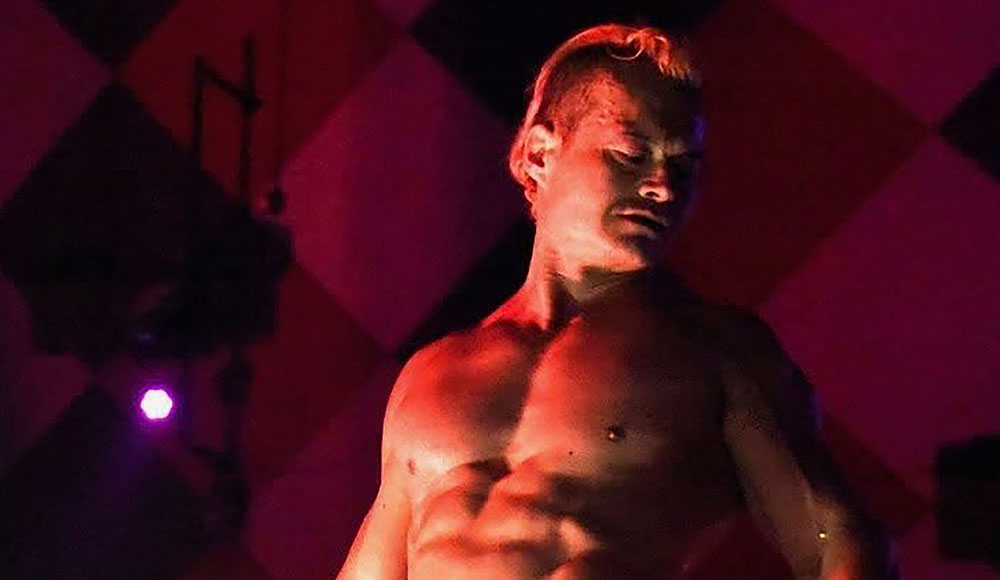 Bare-chested man posing on a stage, with dramatic lighting