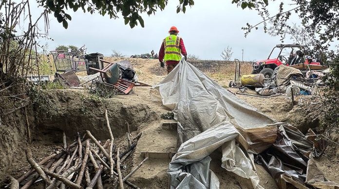 Pushed Out NEWS photo A worker hauls a tarp out of a homeless camp.