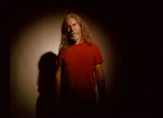 Go Tell It on the Pink Mountaintops Man against a black background wearing a red shirt with a light shining on him