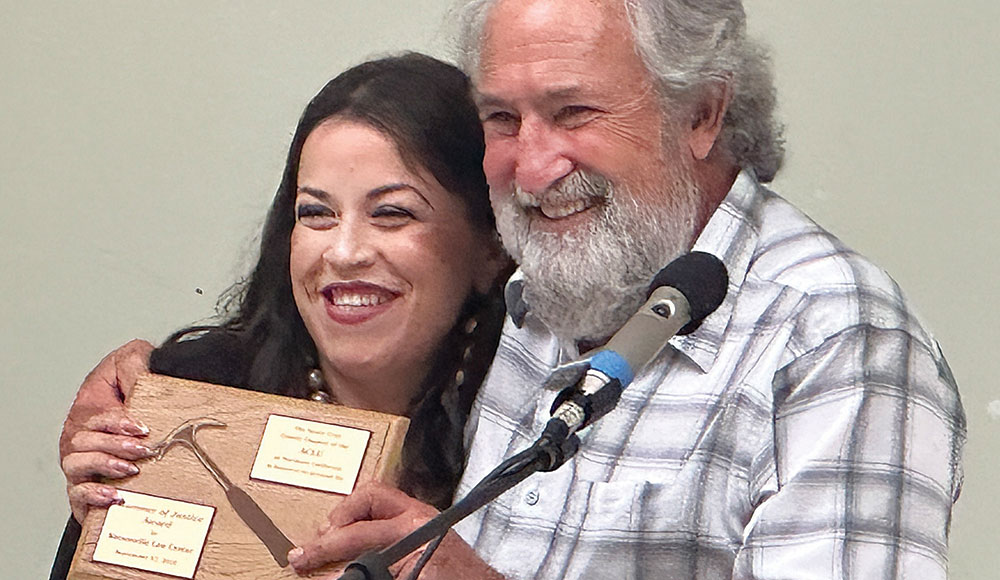 Man and woman at an awards event, woman holding plaque