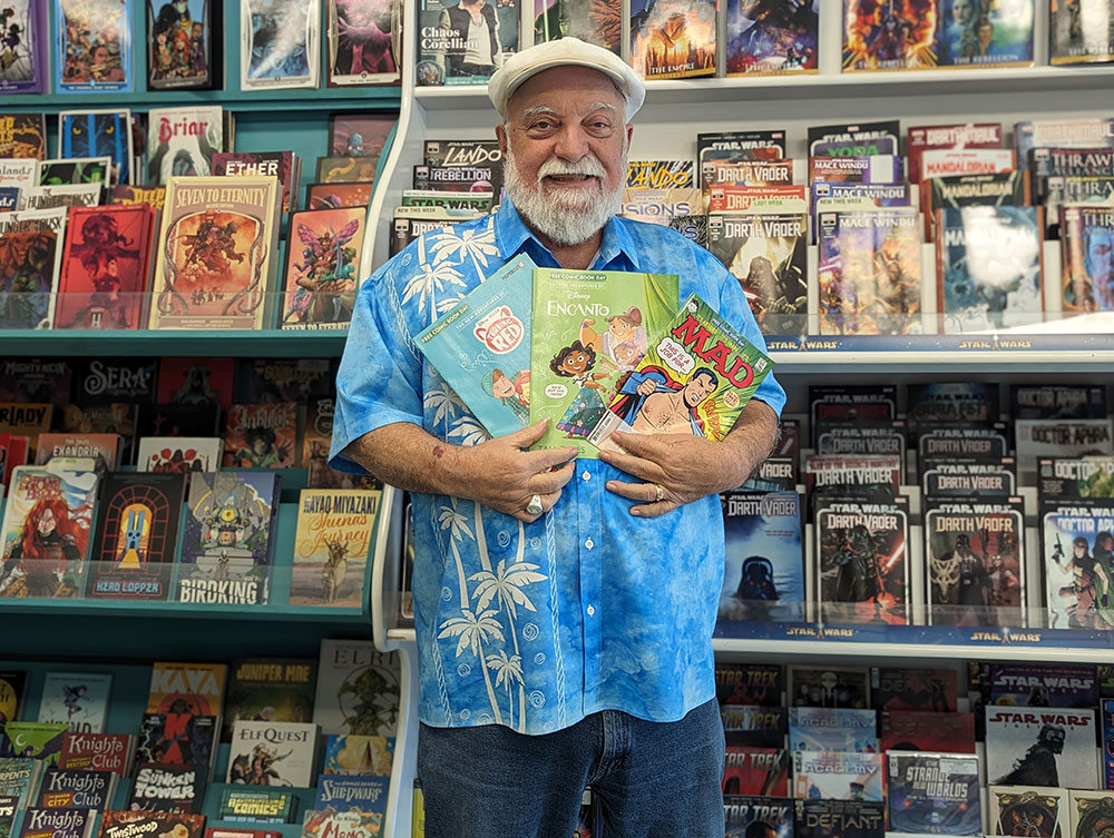 Man holding comic books in front of racks of comic books