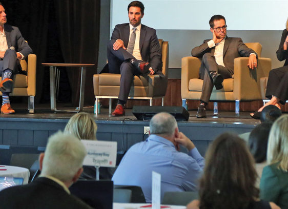 Weighing in at the State of the Region Four people seated on a stage and speaking in front of a crowd