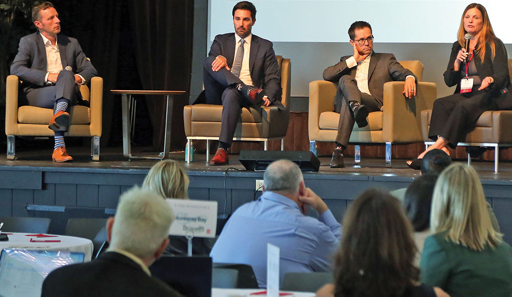 state-of-the-region Four people seated on a stage and speaking in front of a crowd