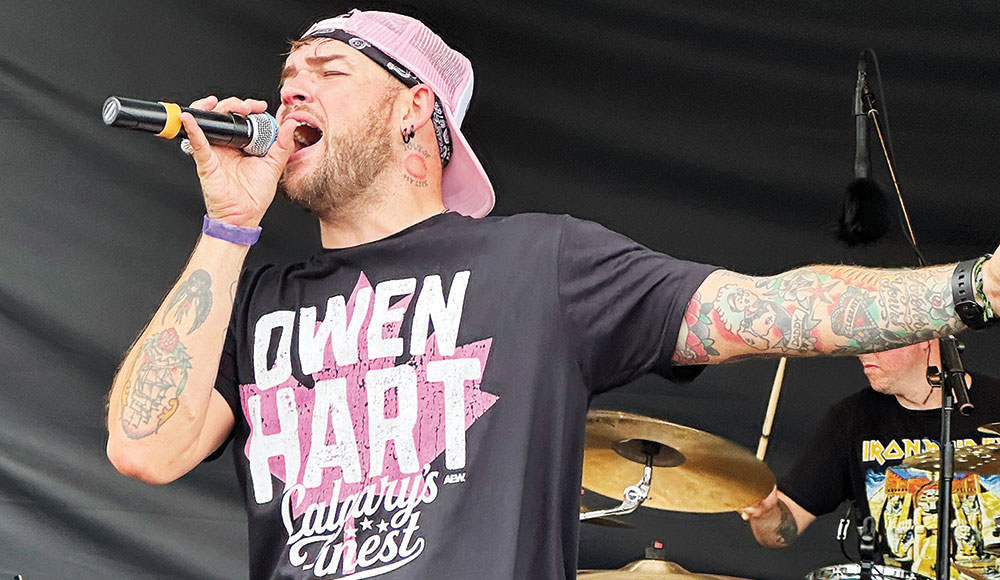 Singer James Durbin singing onstage in an Owen Hart t-shirt and backwards cap.