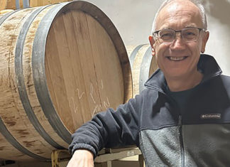 Pinot Pop-up Winemaker Tony Craig dressed casually in a dark hoodieposes with a wine barrel
