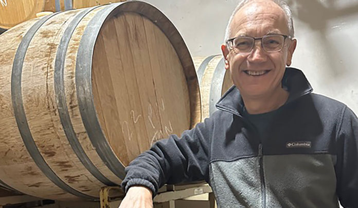 Pinot Pop-up Winemaker Tony Craig dressed casually in a dark hoodieposes with a wine barrel