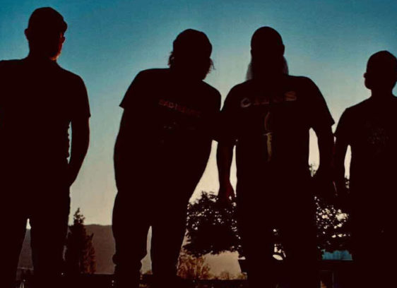 Things to do in Santa Cruz Silhouetted photo of the four members of the rock band Drawing Heaven standing against a dusky blue sky.