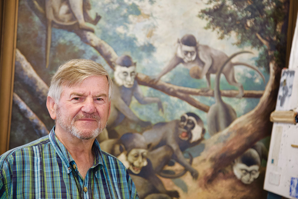 Man standing in front of a large painting depicting monkeys in a forest scene.