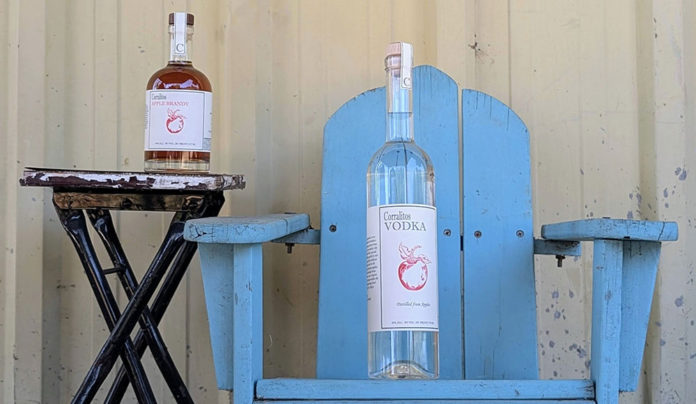 Tasting Sensation Bottles of Corralitos Apple Brandy and Corralitos Vodka displayed on a rustic blue chair and small table outdoors.