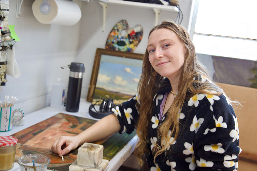 Young woman smiling while working on an art restoration project at a studio desk.