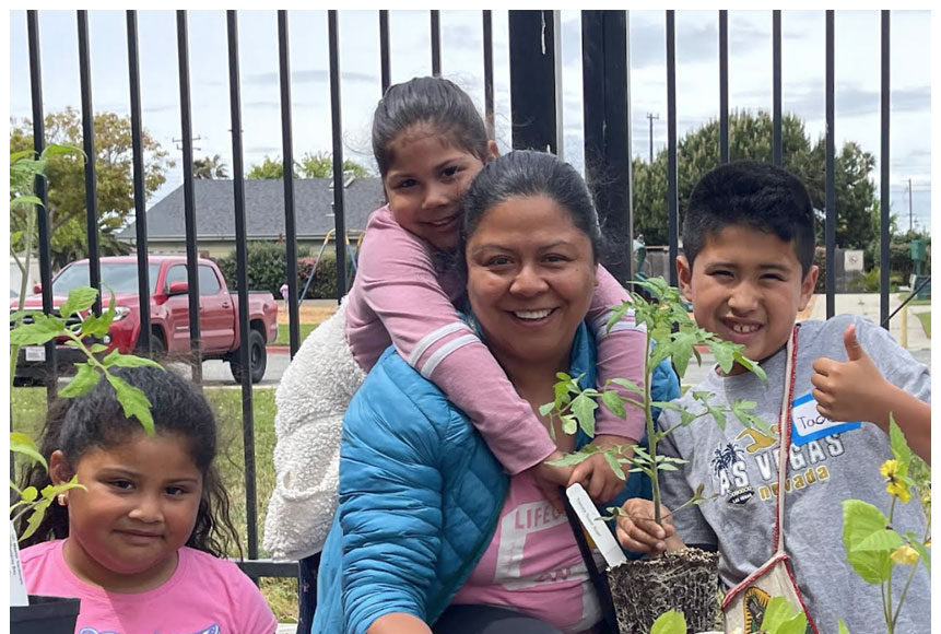 A smiling woman and three children plant vegetables together in portable grow bags during a Monterey Bay Master Gardeners workshop.