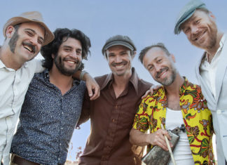 Digging Deep Roots The California Honeydrops band members stand together smiling outdoors, arms around each other.