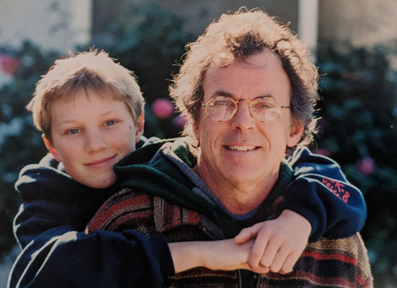Final Exam A young Kyle Thiermann hugs his father Eric Thiermann from behind in a sunlit outdoor photo.