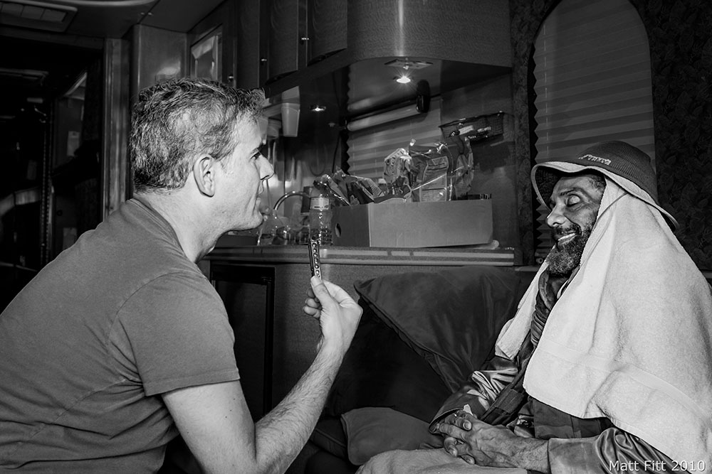 In a black-and-white photo, author John Malkin (left) holds a microphone while talking to Bad Brains leader H.R. Both men in profile.