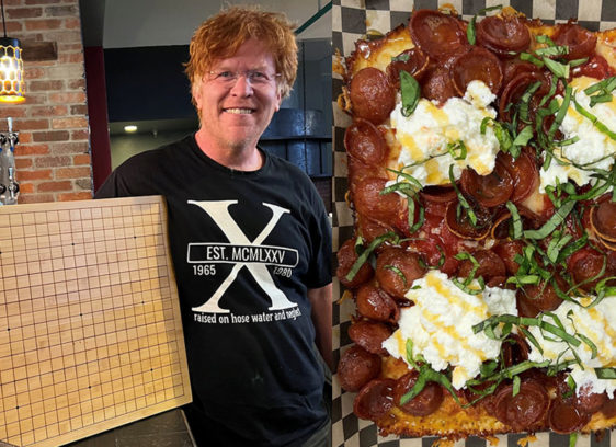 Mission Critical A man at d20 Pizza smiles and holds a wooden Go board beside a Detroit-style pepperoni pizza topped with ricotta and fresh basil.