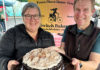 Switch It Up A smiling woman and man hold a chocolate layer cake with chai meringue at the Switch Bakery booth at a local farmers market.