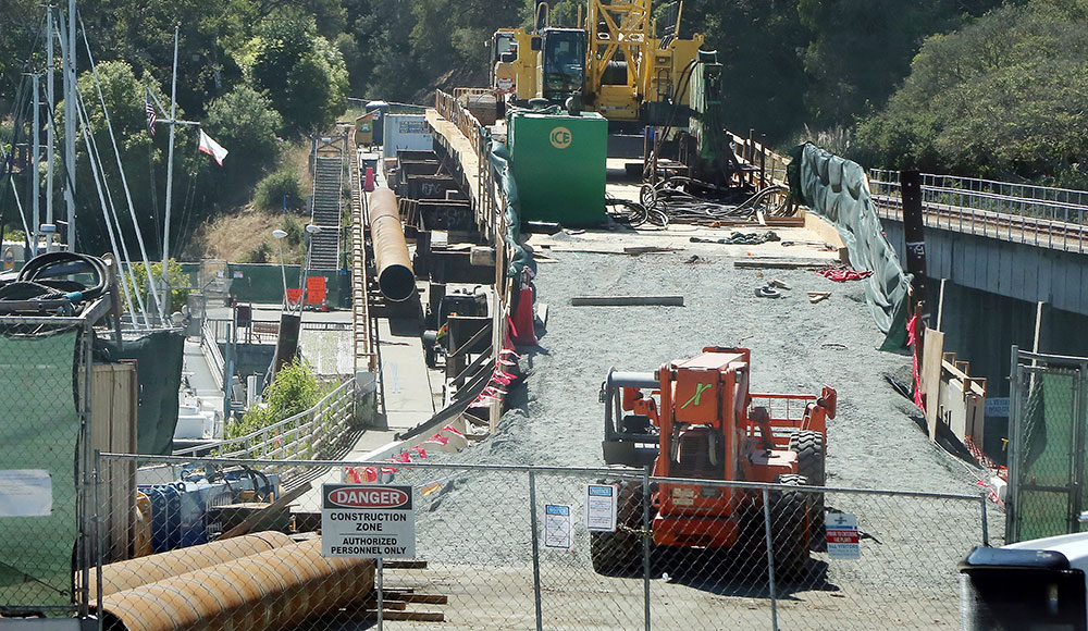 Construction equipment and materials sit atop the closed Murray Street Bridge in Santa Cruz, with fencing and warning signs blocking access.