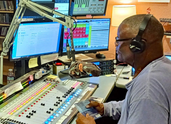 Hear Here Man hosting a live radio show at KSQD, sitting at a control board with headphones on.