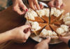 Healthy Holidays Hands from multiple people reach in to take slices of a pumpkin pie topped with whipped cream at a holiday gathering.