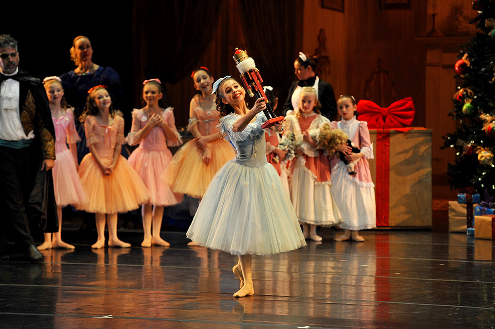 A young ballerina portraying Clara lifts the Nutcracker doll during a Santa Cruz ballet performance.