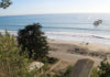 Fortifying the ‘Blue Wall’ A high bluff overlooks Seacliff State Beach with waves rolling onto the sand and the remains of the S.S. Palo Alto visible offshore on a clear, sunny day.