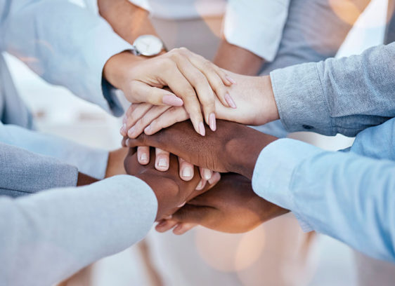 Science of Spirituality A diverse circle of people place their hands together in a stack, symbolizing unity, connection, and mutual support.