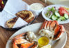 Ocean’s Bounty A plate of freshly cooked Dungeness crab served with melted butter sits beside bowls of clam chowder and a green salad, with toasted garlic bread in a basket on a wooden table.
