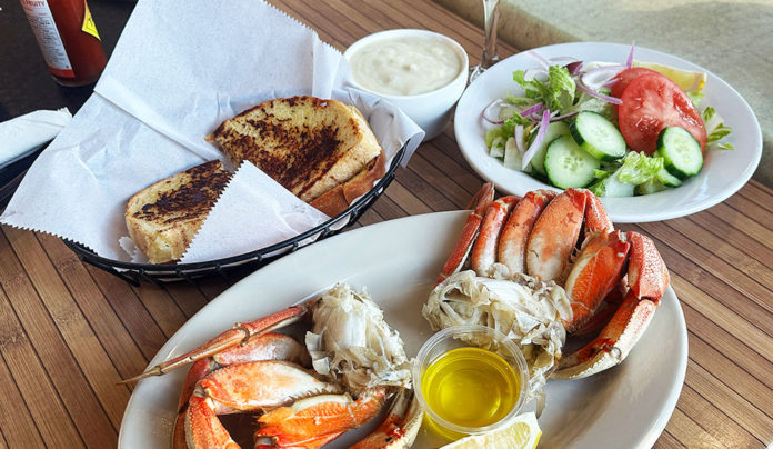 Oceanโs Bounty A plate of freshly cooked Dungeness crab served with melted butter sits beside bowls of clam chowder and a green salad, with toasted garlic bread in a basket on a wooden table.