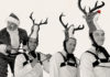Mex-Mas Cheer El Vez dressed as Santa Claus playfully posing behind three performers wearing reindeer costumes with antler hats.