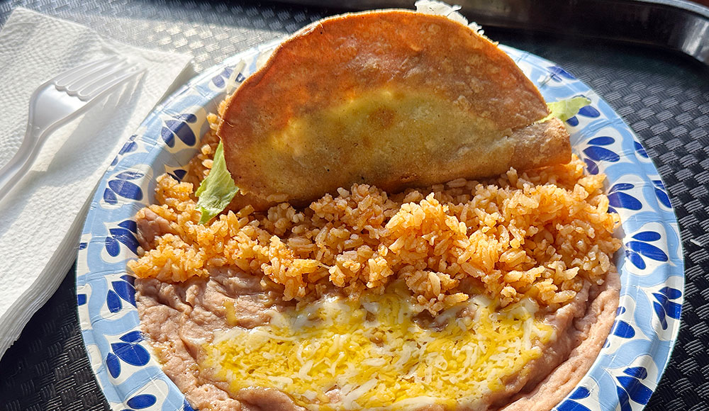 Shredded beef crispy taco served with Mexican rice and refried beans topped with melted cheese at Las Palmas Taco Bar.