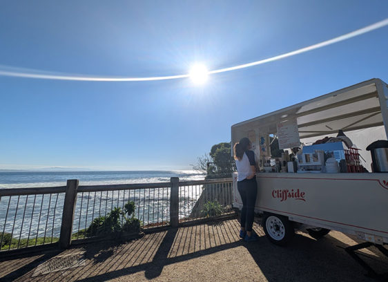 Twelve Bites of Christmas A woman orders coffee from the Cliffside trailer overlooking the ocean on a bright, sunny day.