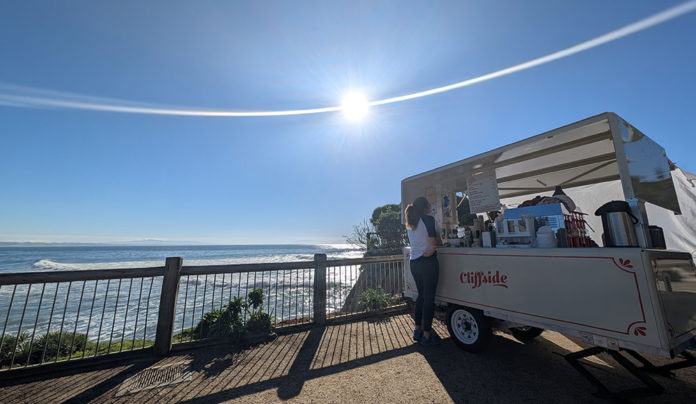 Twelve Bites of Christmas A woman orders coffee from the Cliffside trailer overlooking the ocean on a bright, sunny day.