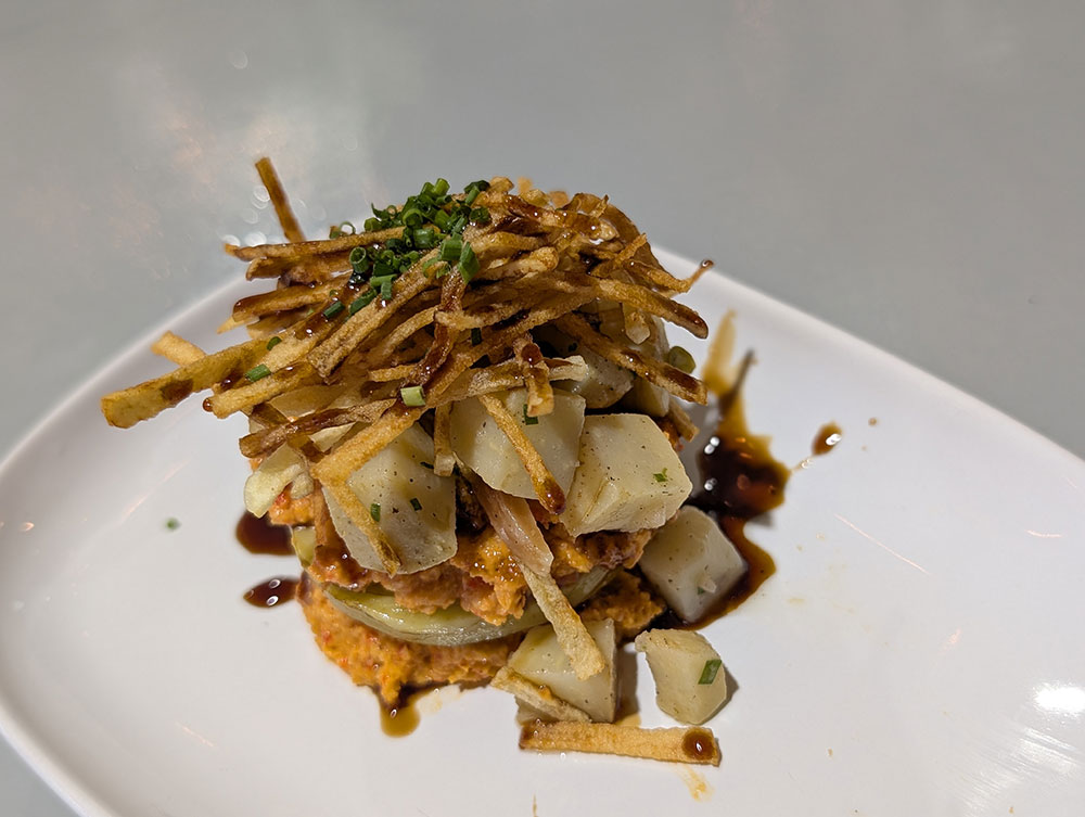 A plated stack of Food Lab’s artichoke ensalada topped with crispy shoestring potatoes and herbs.