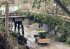 Tracks Derailed A tractor clears mud beneath a storm-damaged rail bridge covered with fallen trees near New Brighton.