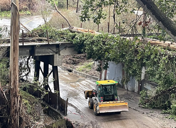 Tracks Derailed A tractor clears mud beneath a storm-damaged rail bridge covered with fallen trees near New Brighton.